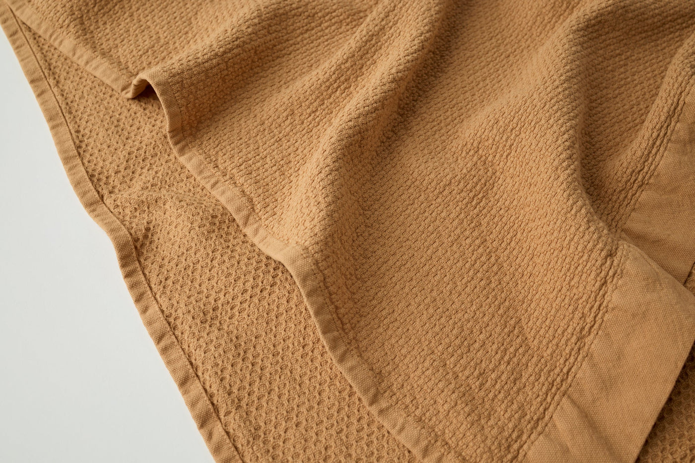 Close-up of camel waffle-weave towel corner showing stitched border detail.