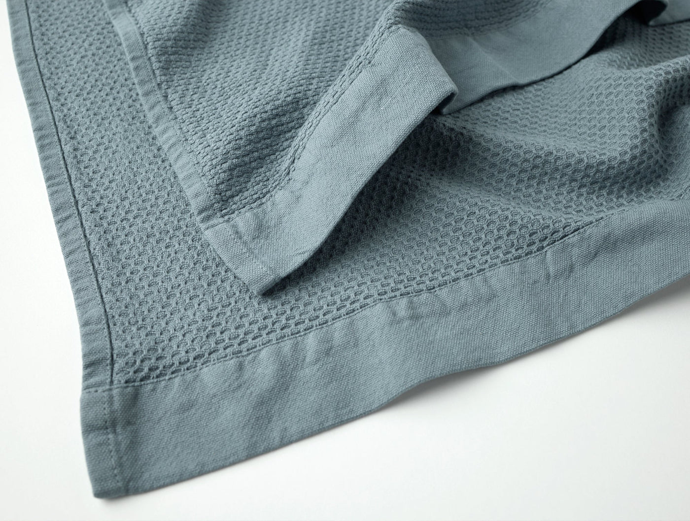 Close-up of Coyuchi Adriatic bath towel corner, slate blue waffle texture with woven border hem.