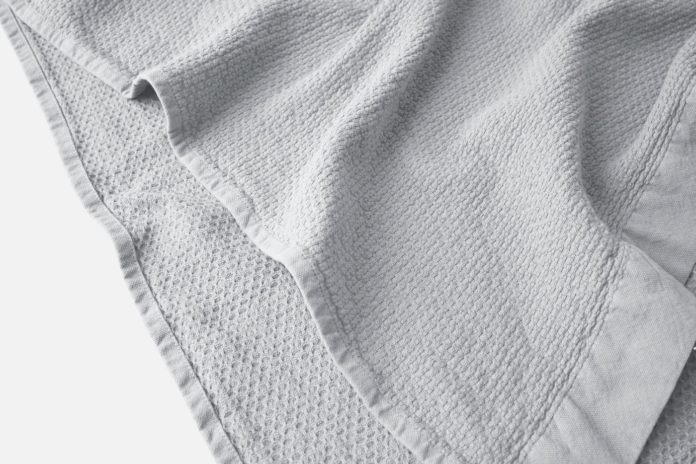 Close-up of Coyuchi Adriatic towel hem detail showing waffle texture and bordered edge in pale grey.