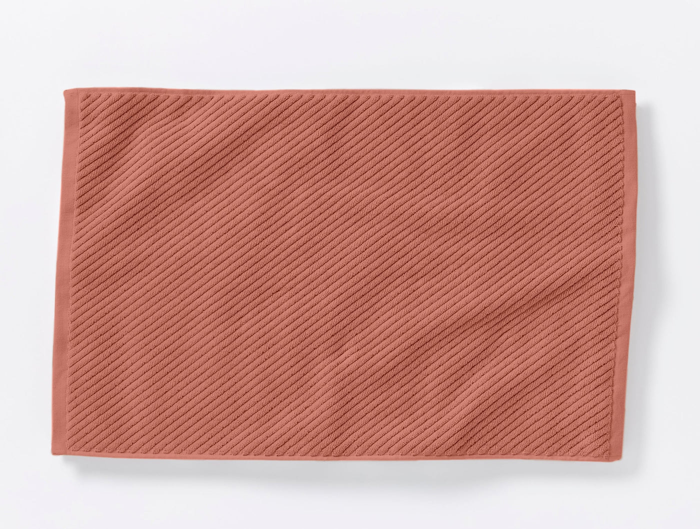 Terracotta twill-weave bath rug laid flat, showing diagonal ribbed texture.
