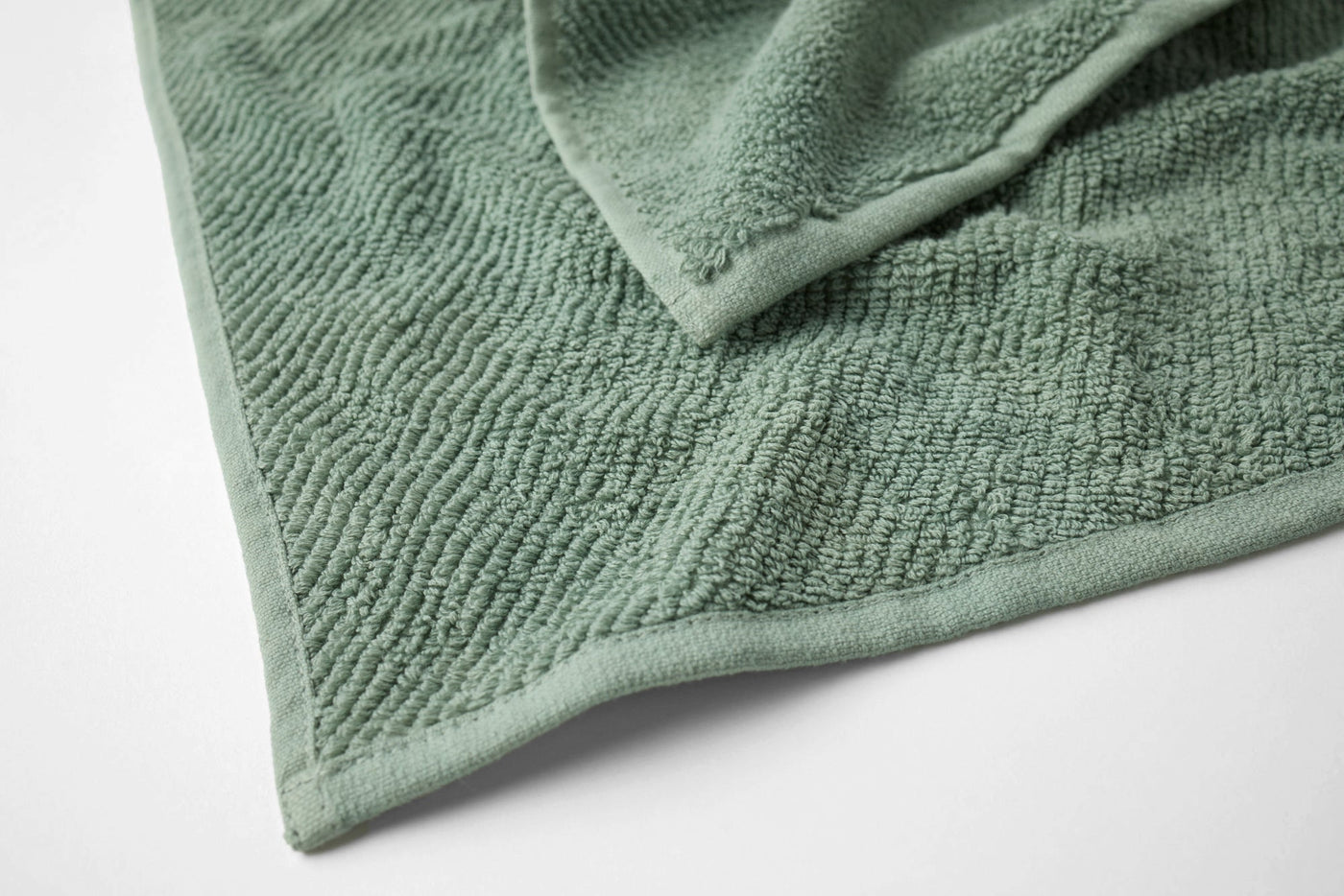 Close-up of sage green terry bath sheet corner showing plush pile texture and hem detail.