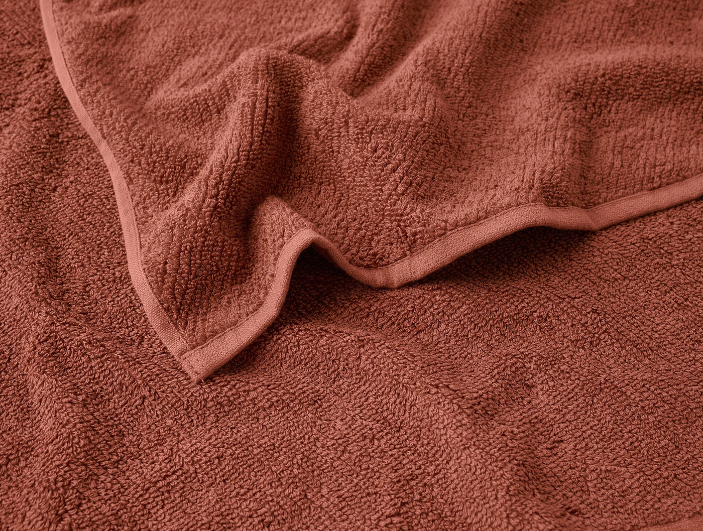 Close-up of terracotta Coyuchi Air Weight towel hem, showing plush looped texture and folded edge.