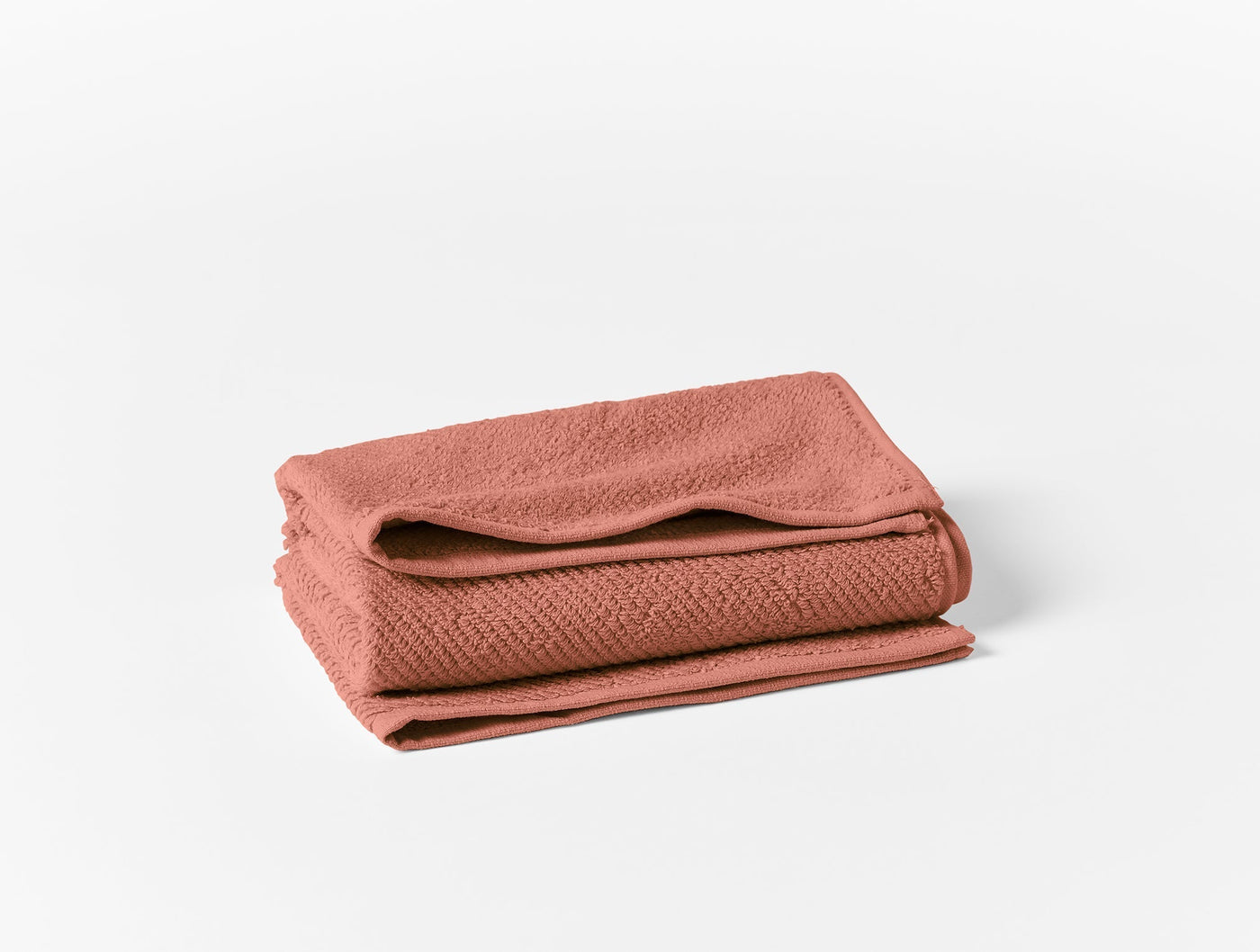 Folded terracotta oversized hand towel with subtle waffle weave texture, stacked on white background.