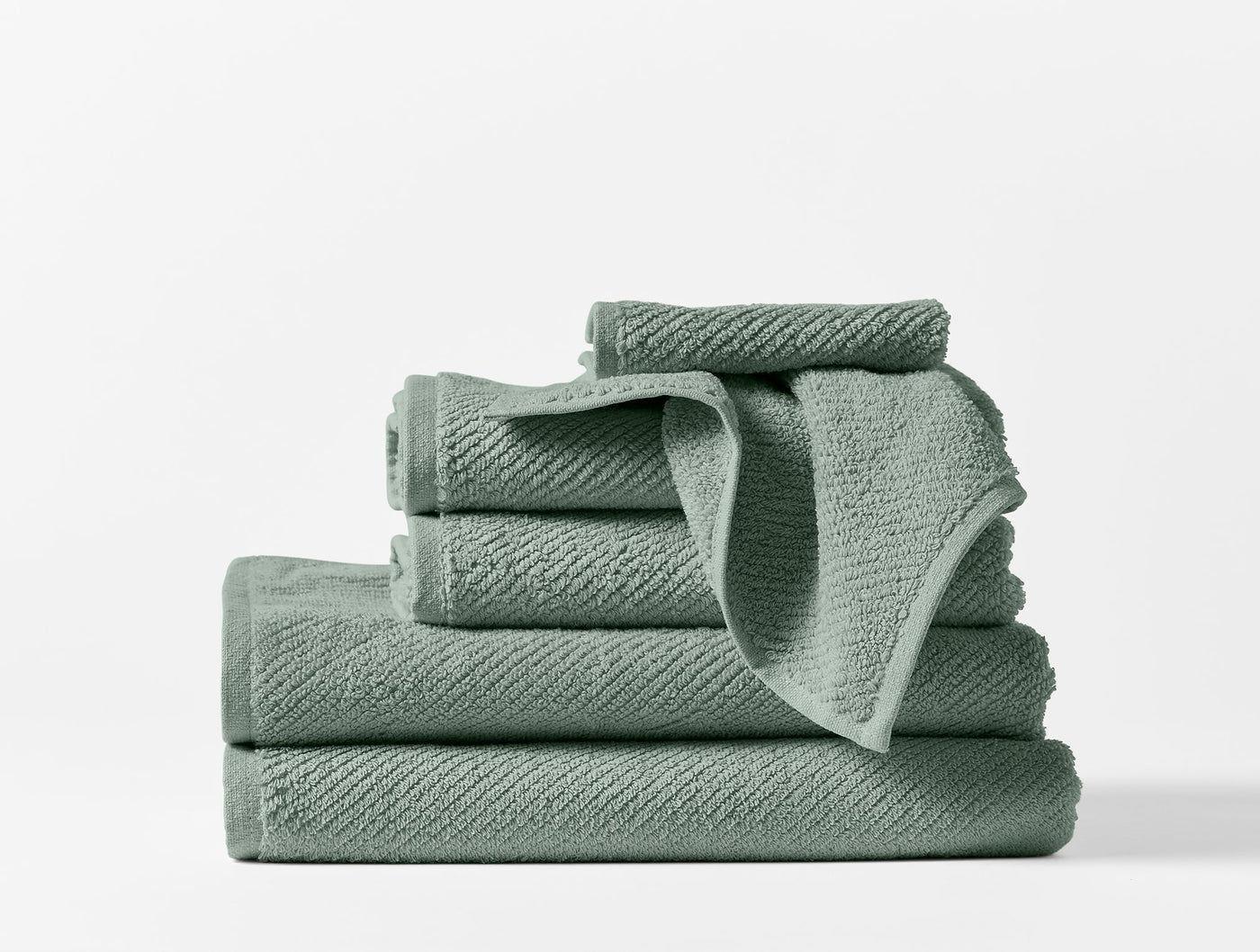 Stacked sage Coyuchi Air Weight towel set showing varied sizes and textured weave detail.