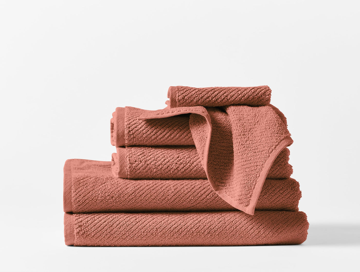 Stacked terracotta Coyuchi Air Weight towels showing varied sizes and ribbed texture detail.