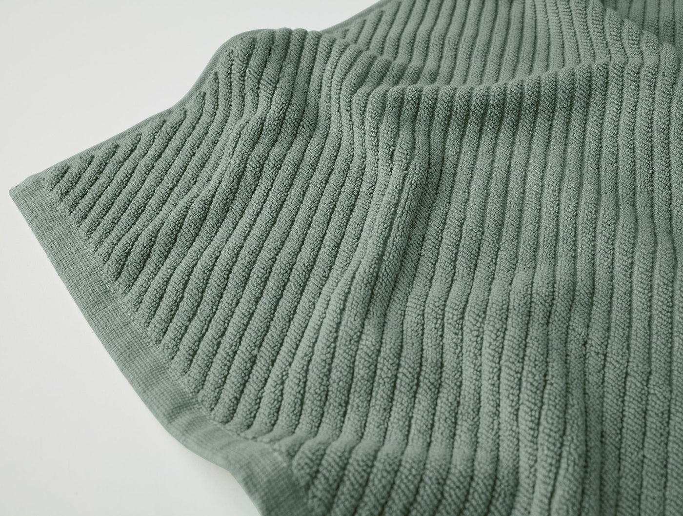 Close-up of Coyuchi Air Weight bath rug corner, showing ribbed cotton weave in sage green.