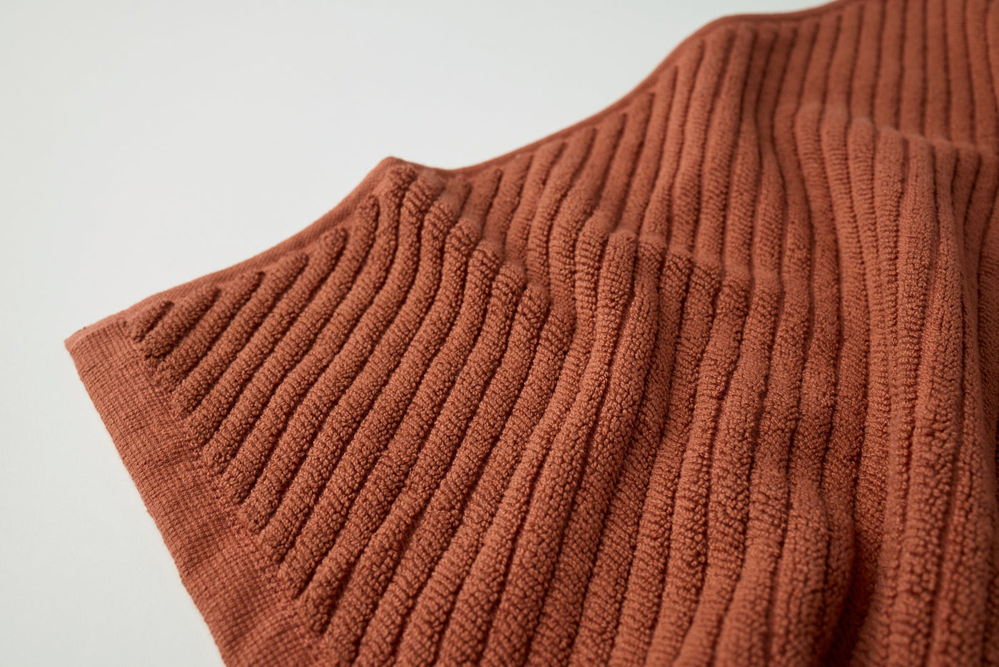 Close-up of Coyuchi Air Weight bath rug in terracotta, showing ridged organic cotton weave texture.