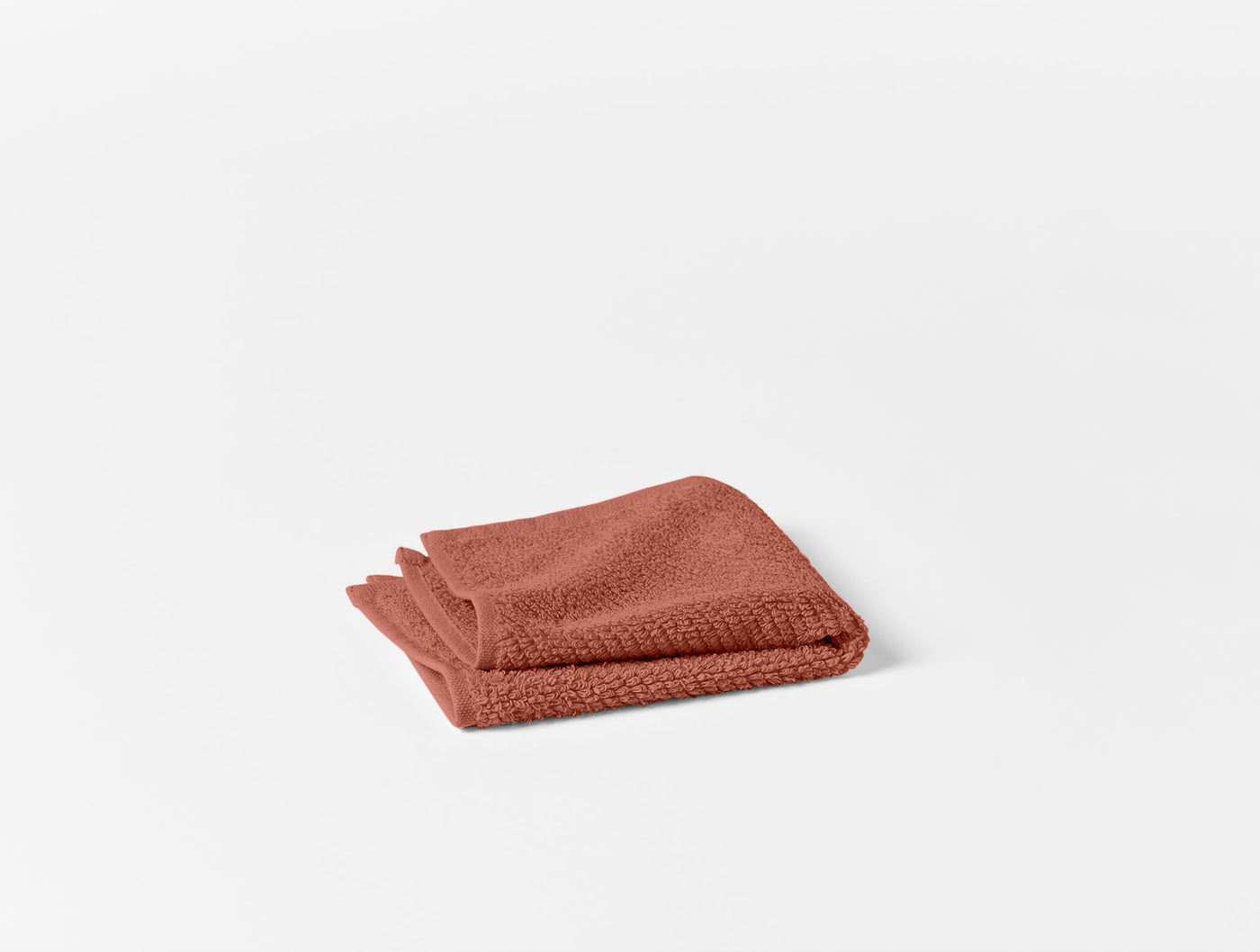 Coyuchi Air Weight wash cloth folded in terracotta, showing textured cotton weave.