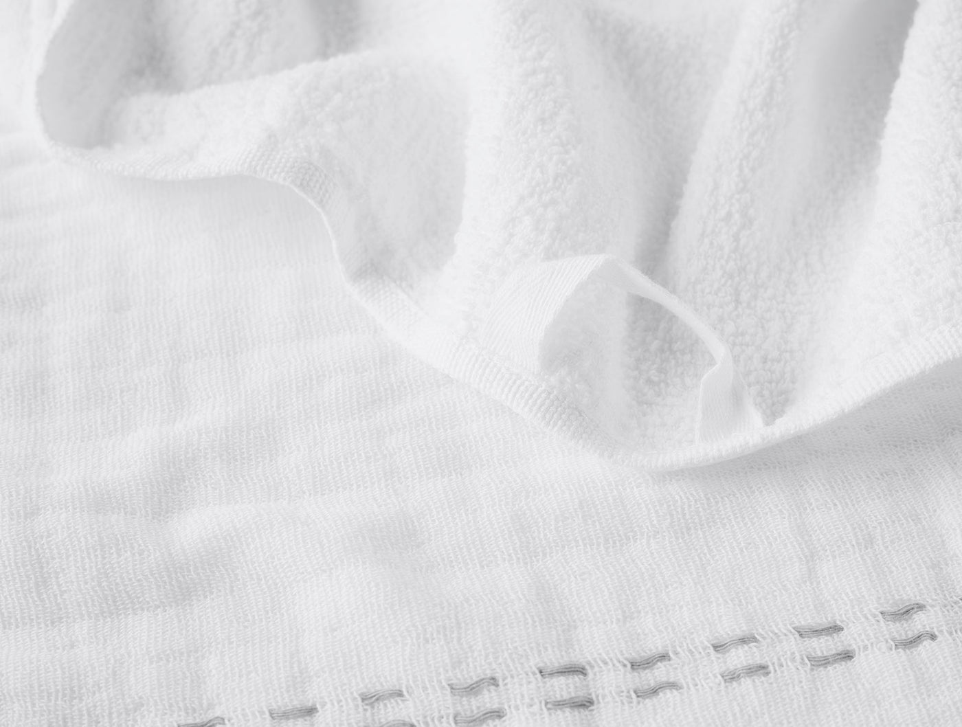 Close-up of white terry hand towel hem with delicate ladder-stitch border detail.