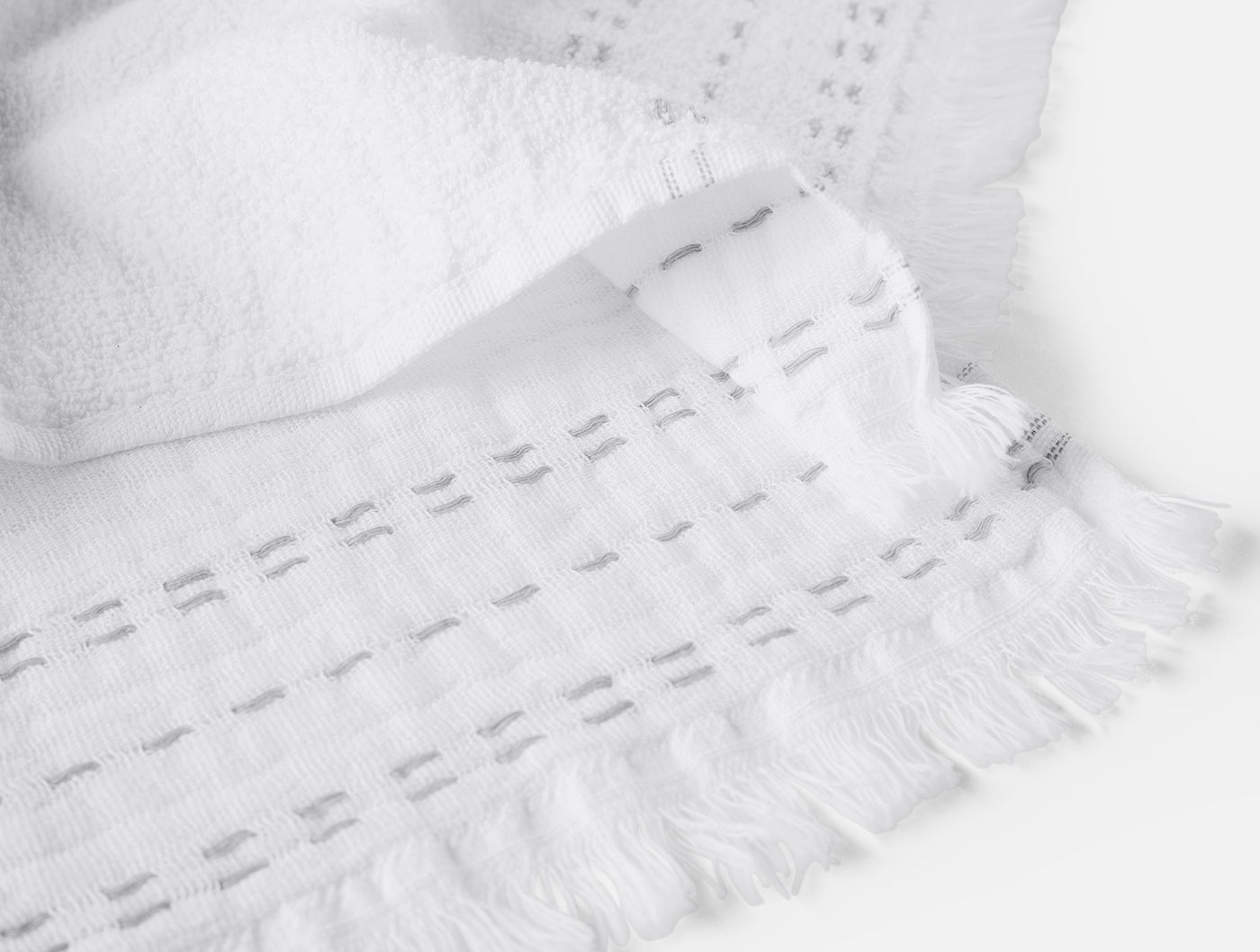 Close-up of Coyuchi Alder hand towel fringe trim and woven border detail in white.
