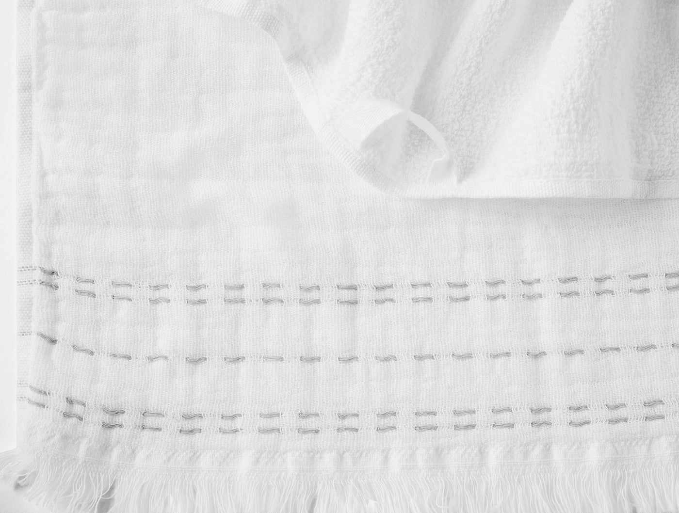Close-up of white Coyuchi Alder hand towel showing woven grid texture and fringe hem detail.