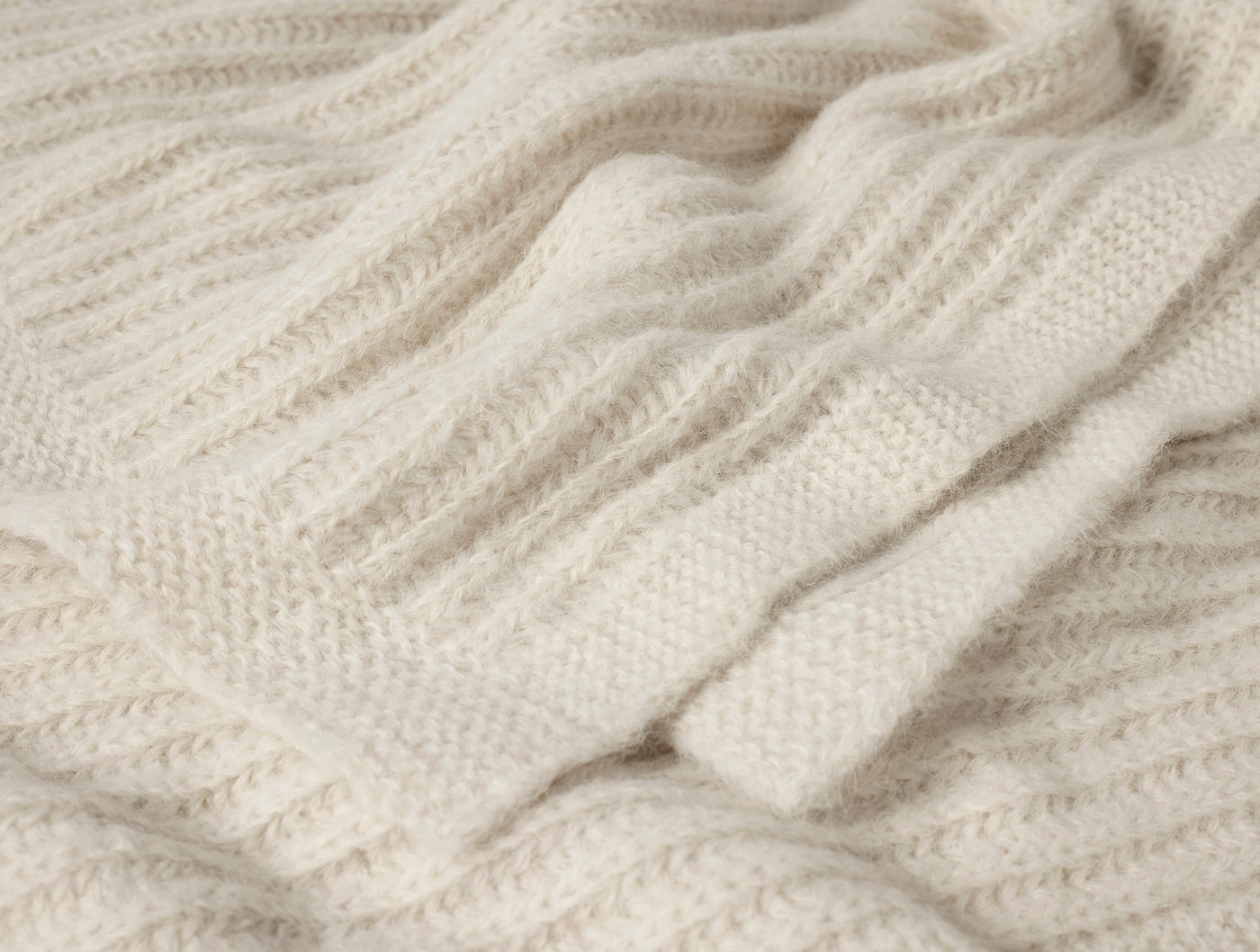 Close-up of ivory Coyuchi Andes Suri Alpaca Knit throw showing ribbed texture and soft fringe.