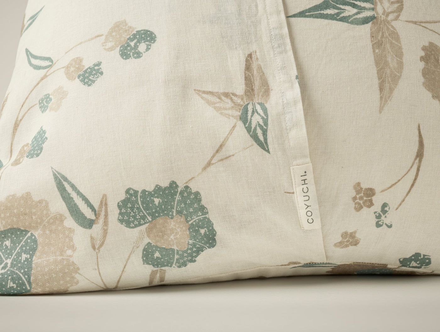 Close-up of Coyuchi Aurora Print sham showing sage and taupe floral pattern with woven label.