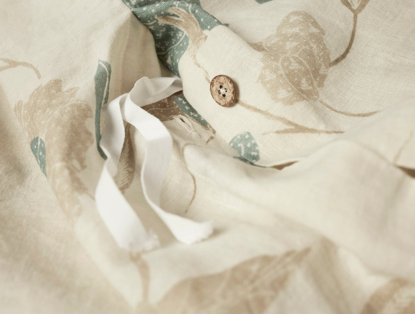 Close-up of Aurora duvet cover button closure, ivory linen with sage botanical print reverse.