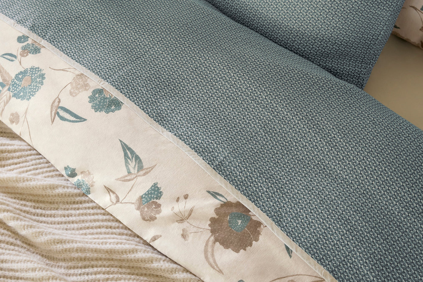 Close-up of teal honeycomb-weave blanket with ivory floral embroidered border detail.