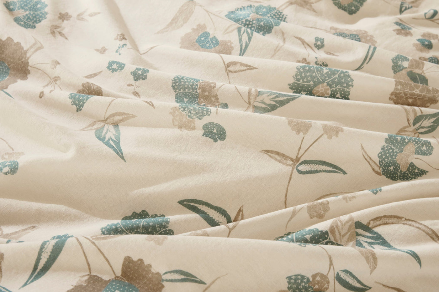 Close-up of ivory cotton fabric with teal and taupe floral print, soft draping folds.
