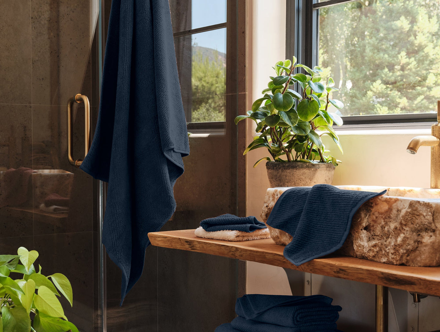 Navy blue Coyuchi Air Weight bath towels styled in a rustic bathroom with stone sink and greenery.