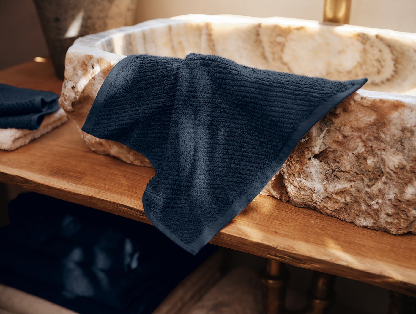 Navy ribbed-texture washcloth draped over a stone basin edge on a wood vanity.