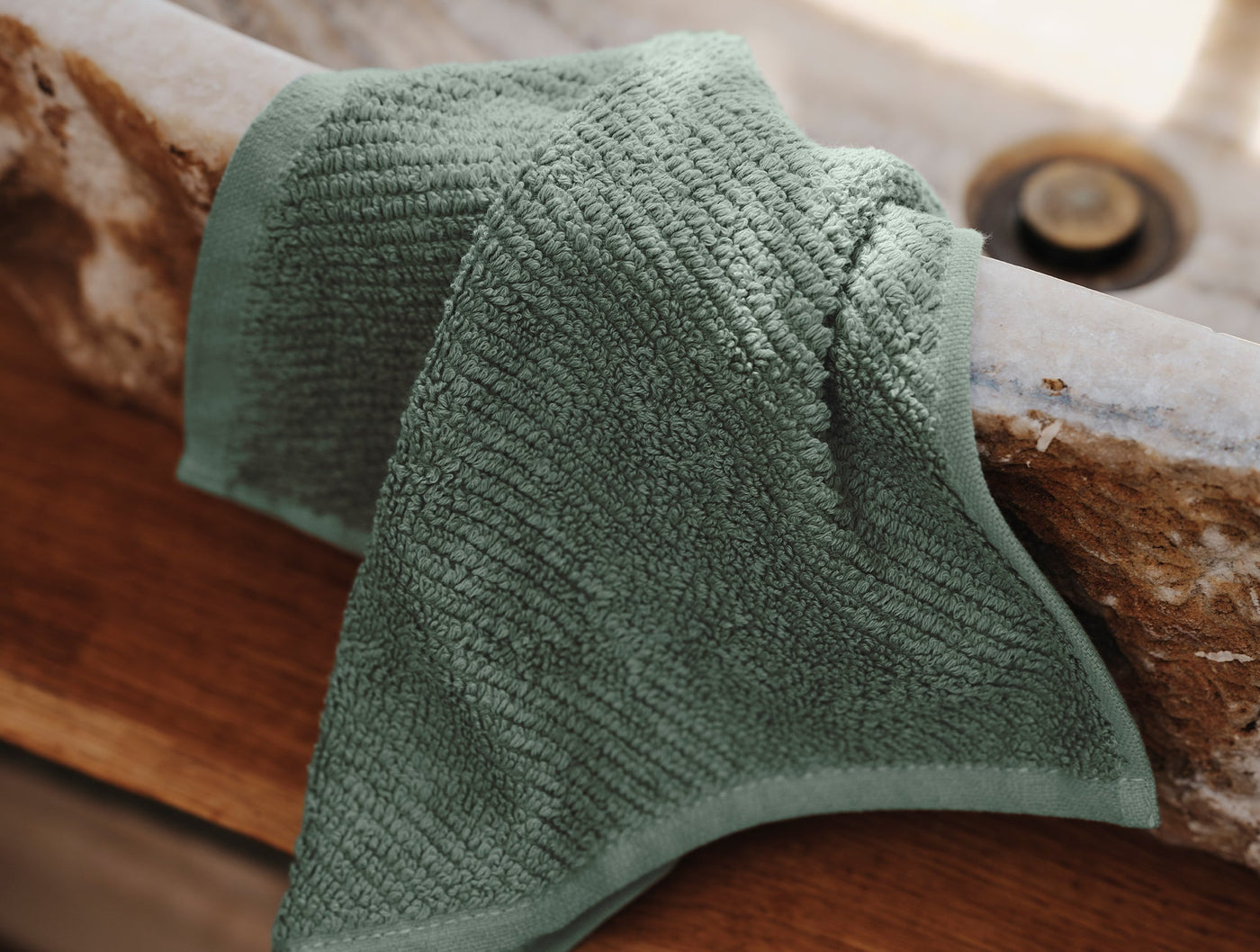 Close-up of sage green Coyuchi Air Weight bath sheet draped over a stone basin edge.