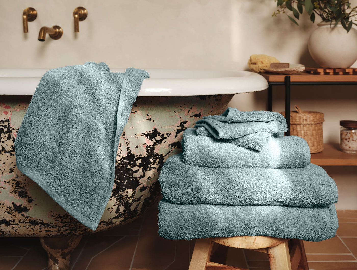 Coyuchi Cloud Loom towel set draped and stacked beside a vintage clawfoot tub in slate blue.