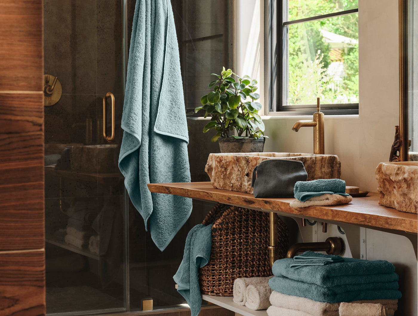 Coyuchi Cloud Loom towels in teal styled in a warm wood bathroom with stone sinks.