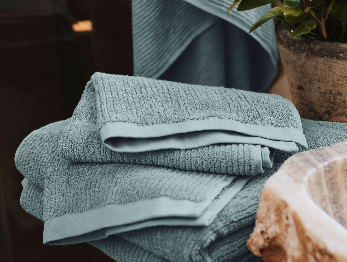 Close-up of stacked slate blue ribbed cotton bath sheets with satin hem detail.