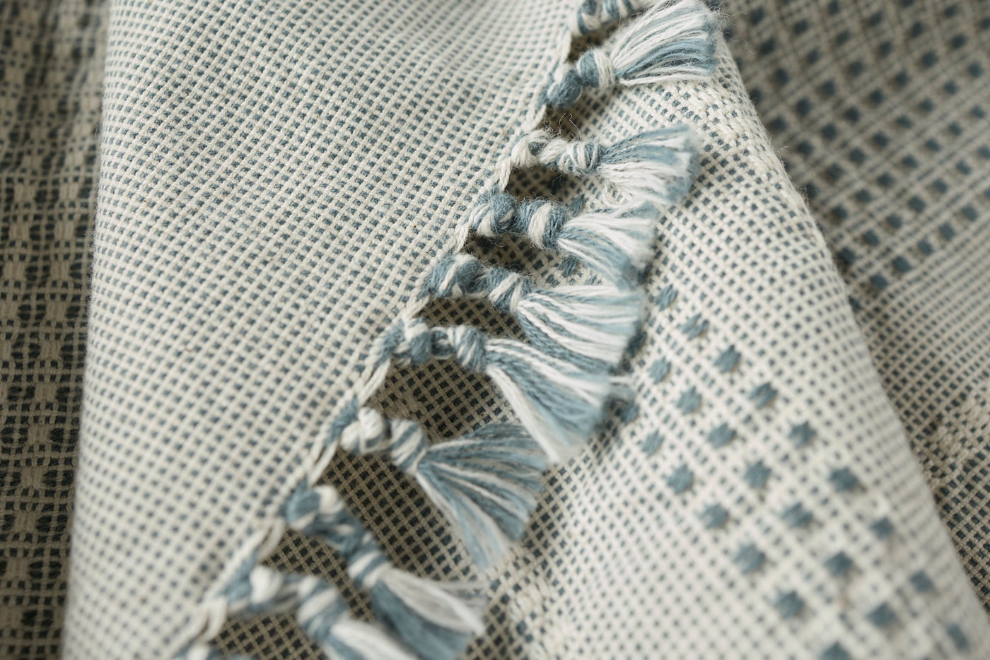 Close-up of Coyuchi Bay hand towel edge with blue fringe trim and woven dot pattern.