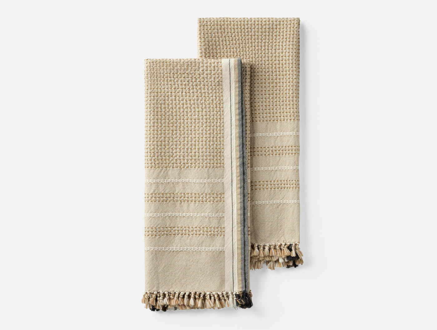 Two folded Coyuchi Bay hand towels in natural with waffle texture, stripe detail, and fringe hem.