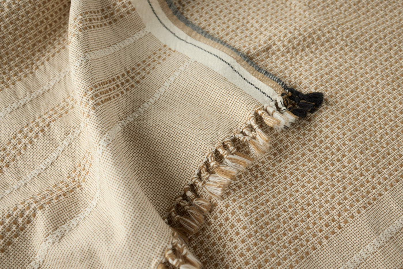 Close-up of natural cotton weave with fringe trim and contrast edge stripe detail.