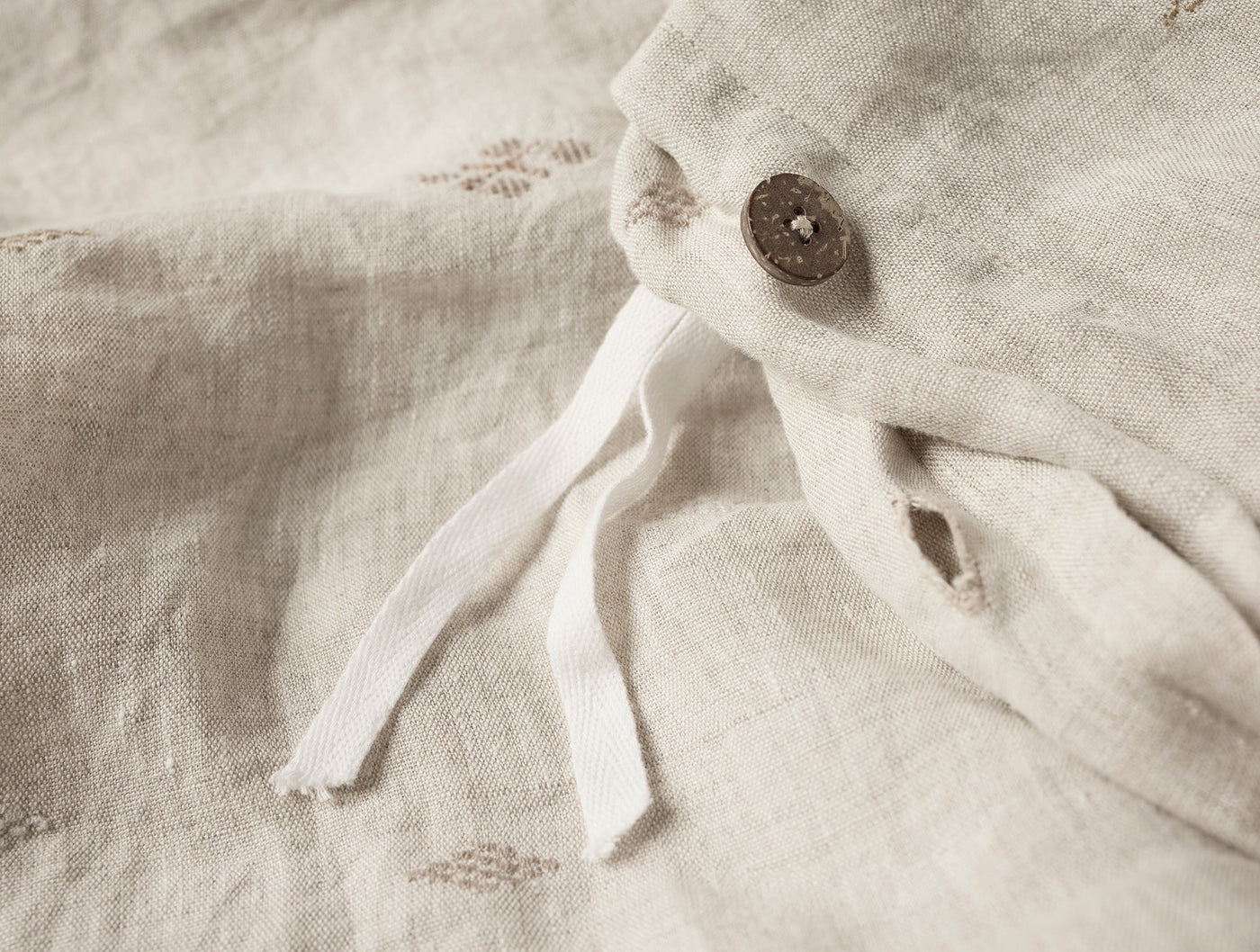 Close-up of coconut shell button and white tie closure on natural linen duvet cover.