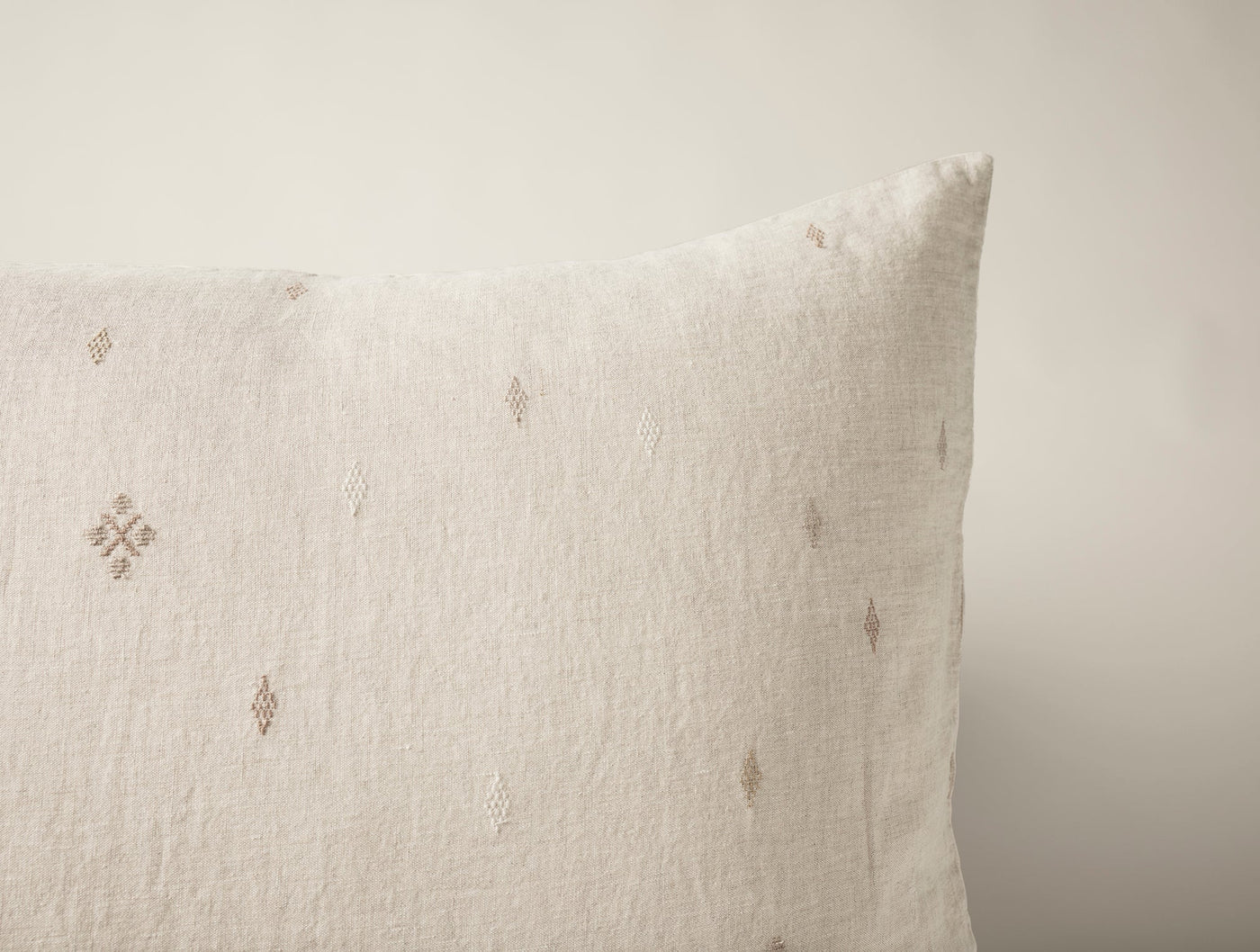 Close-up of ivory linen sham corner with scattered taupe diamond embroidery motifs.