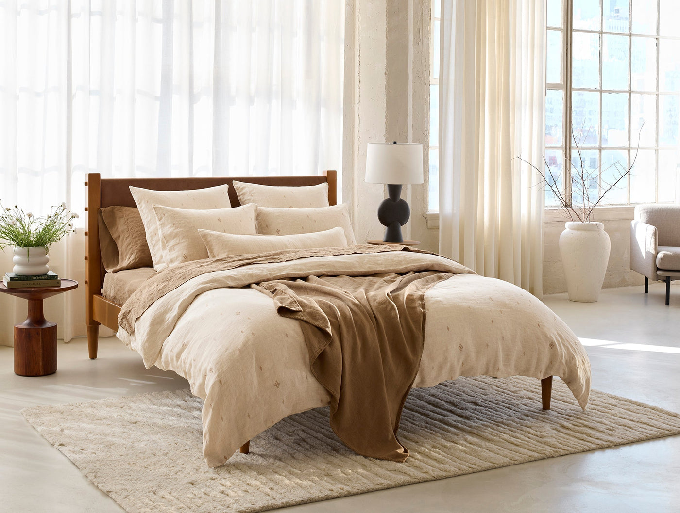 Coyuchi Cambria duvet cover styled on bed with warm sand throw and sheer curtains.
