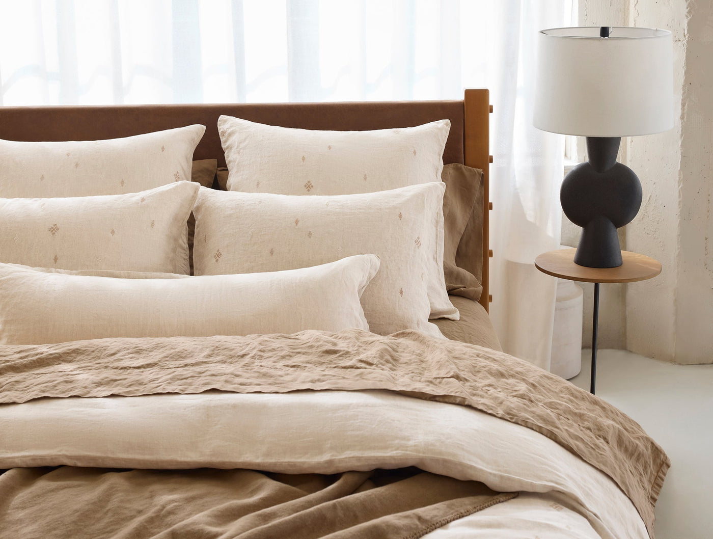 Ivory linen duvet and embroidered shams styled on a bed with warm wood headboard.