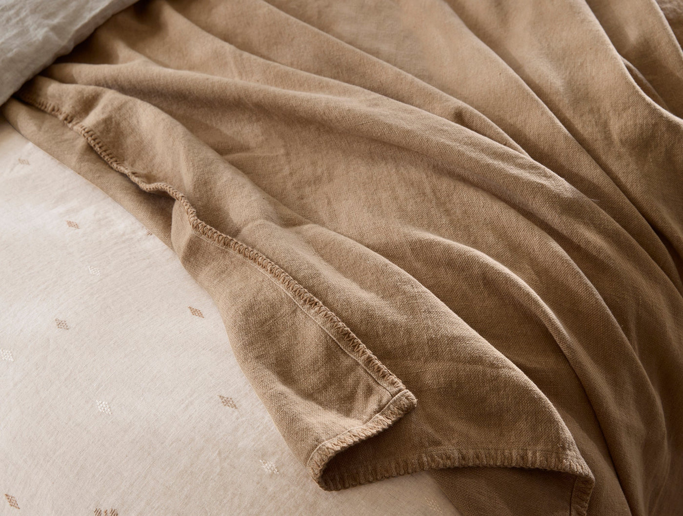 Close-up of Coyuchi Helena camel linen throw hem, draped over bedding showing washed texture.