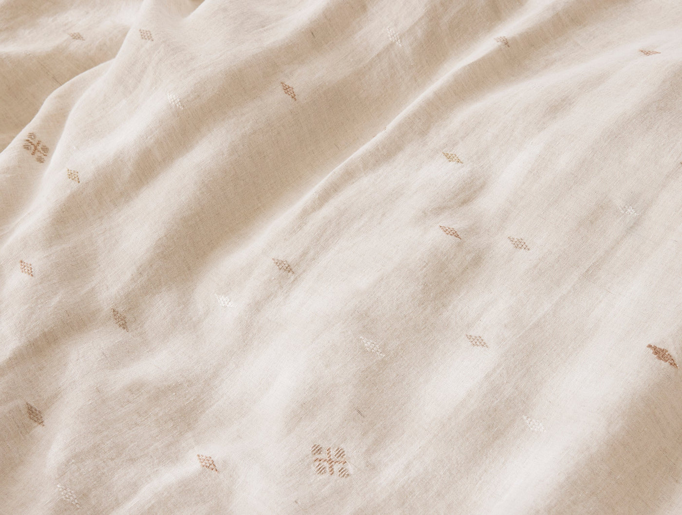 Close-up of ivory linen duvet cover with scattered tan embroidered botanical motifs.