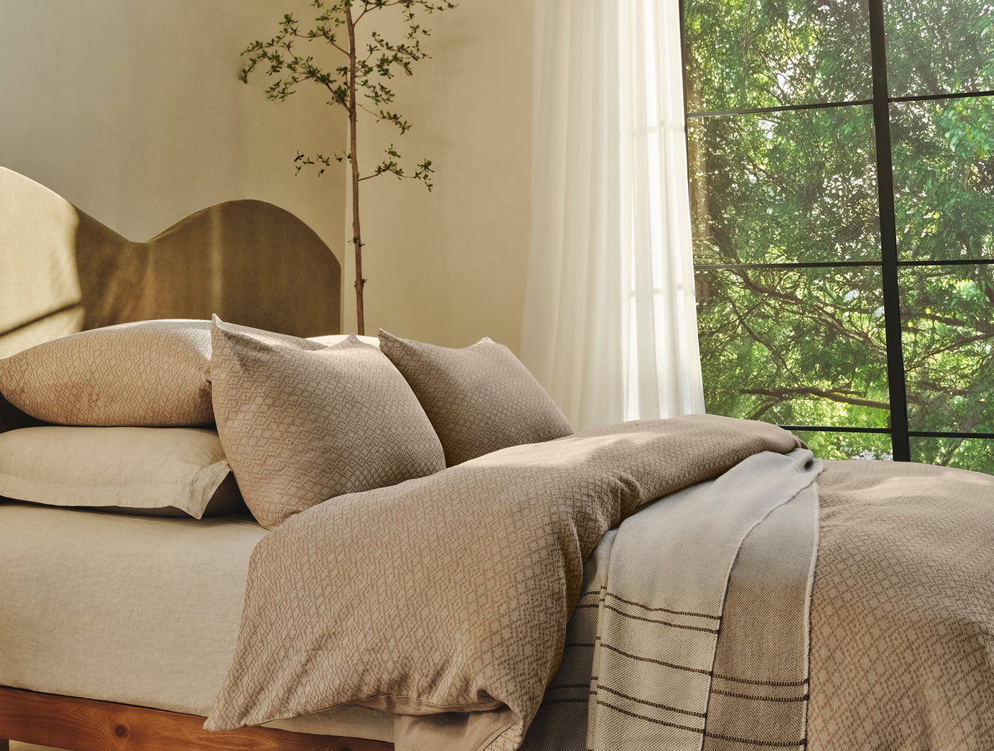 Capitola sham styled on bed with striped throw blanket, natural linen tones, garden window.