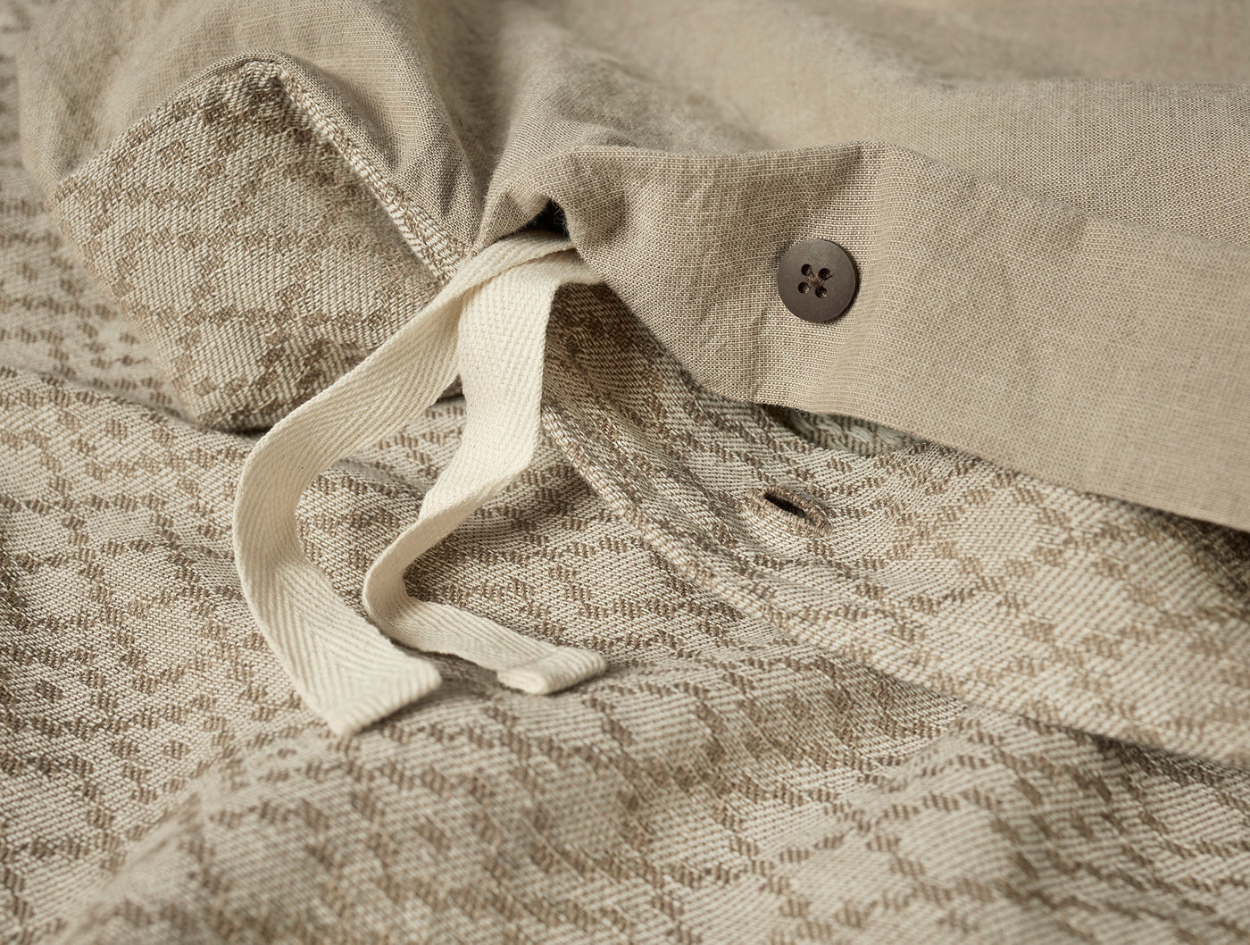 Close-up of duvet cover corner showing interior ties, button closure, and diamond-weave texture in natural linen.