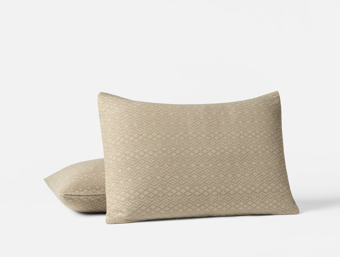 Close-up of two stacked Capitola shams in sand with woven geometric diamond pattern.