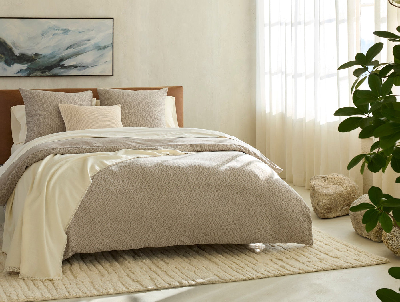 Capitola sham styled on a made bed with ivory sheets in a warm neutral bedroom setting.