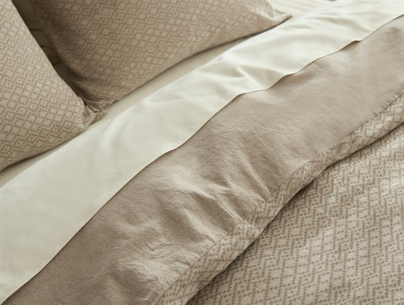 Close-up of Coyuchi Capitola duvet cover hem, showing ivory satin border against taupe diamond-pattern linen.