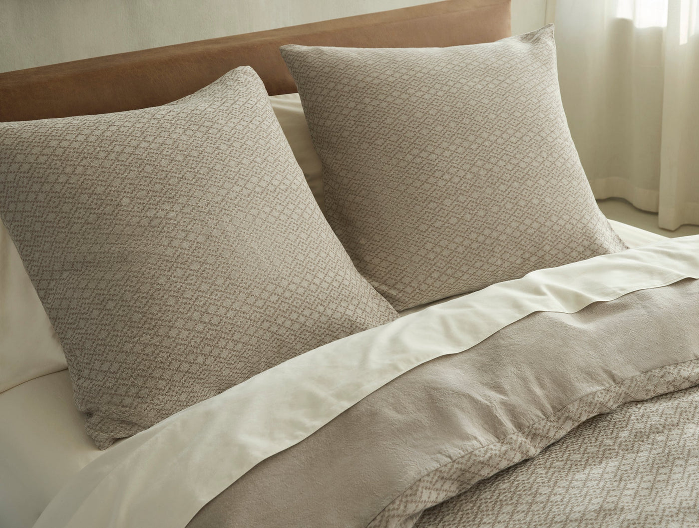 Two taupe Capitola shams with woven diamond pattern on a made bed, natural light.