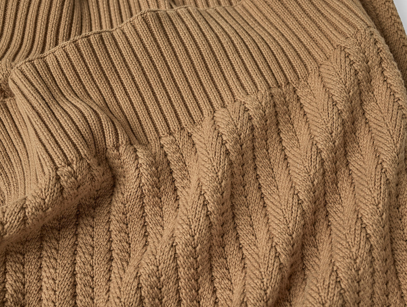 Close-up of Coyuchi Casa Loma Knit Throw showing camel cable-knit weave and ribbed edge detail.