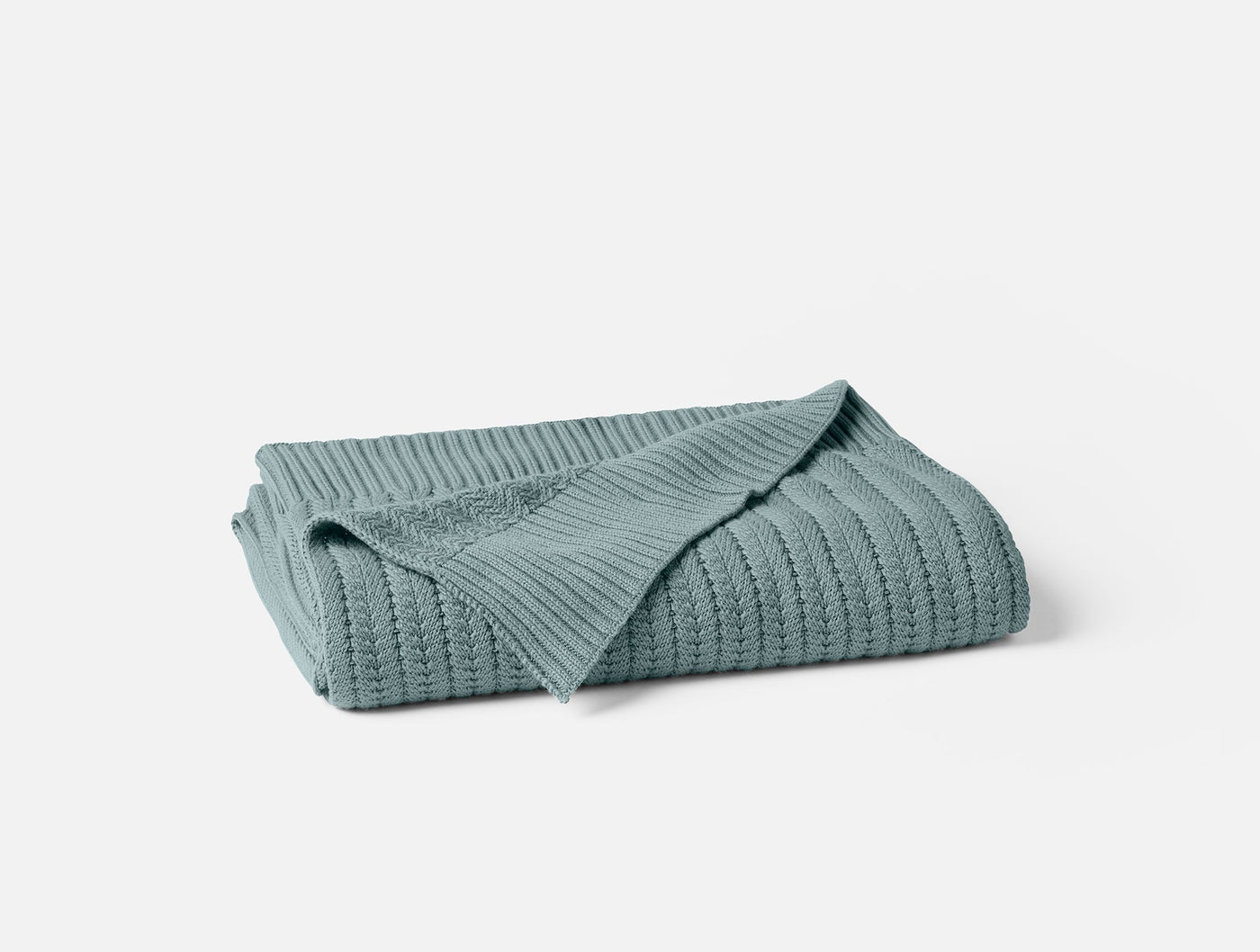 Folded sage green ribbed knit throw, showing textured cable pattern and neatly stacked layers.