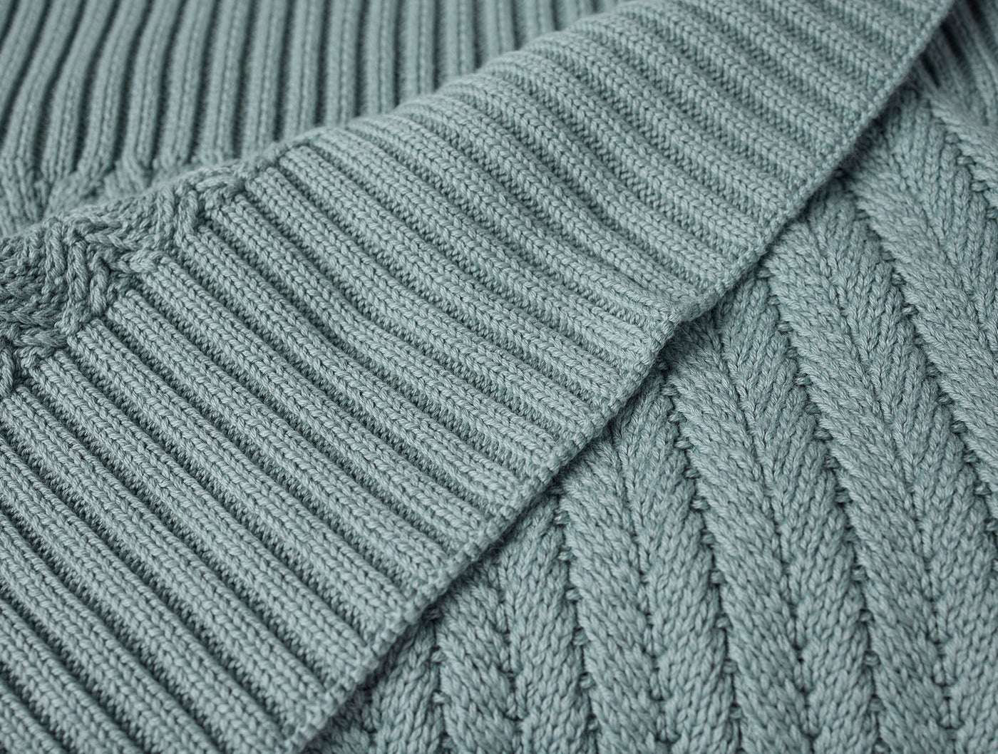 Close-up of Coyuchi Casa Loma Knit Throw in sage, showing ribbed hem and cable-knit texture.
