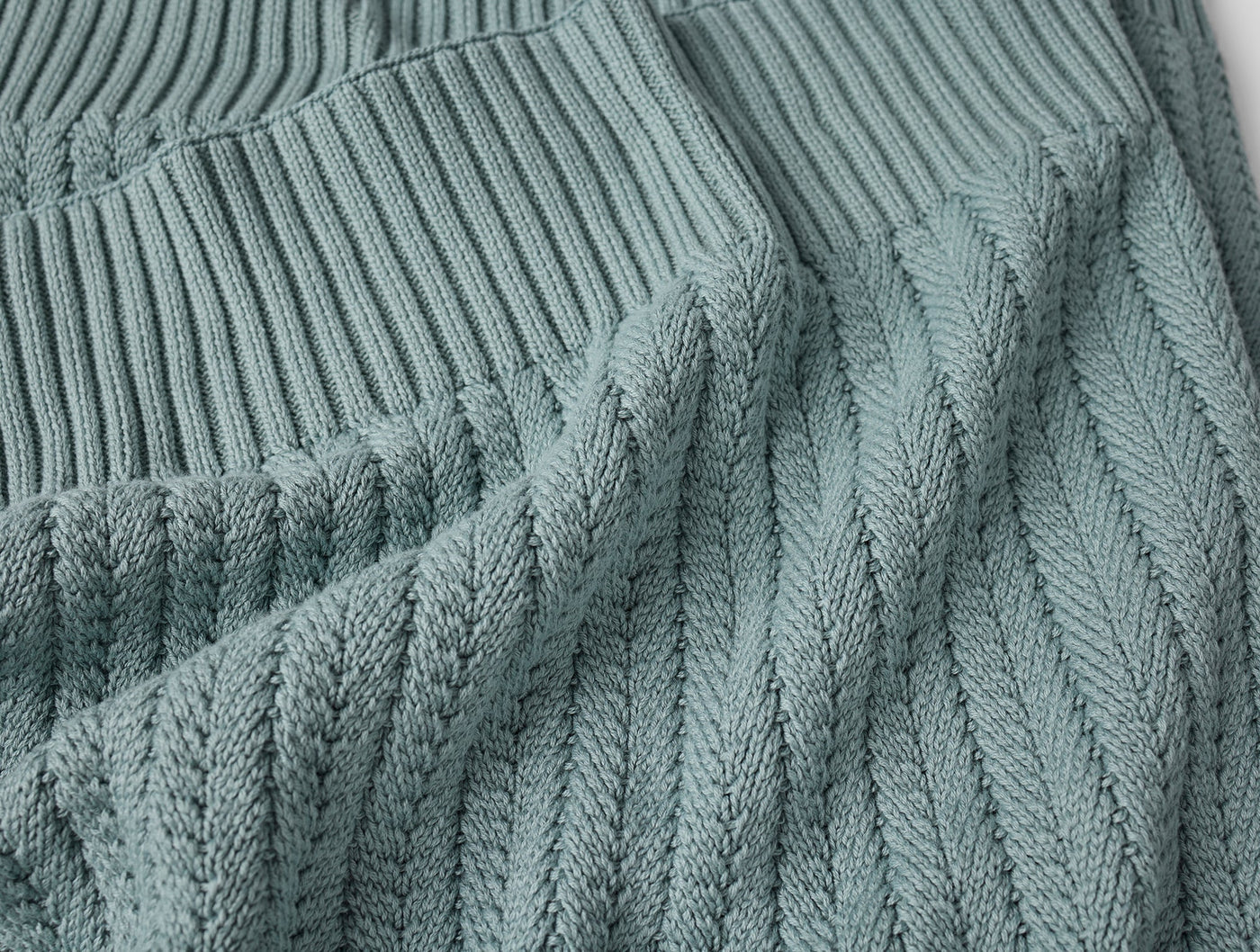 Close-up of sage green cable-knit weave texture and ribbed hem detail on Coyuchi throw.