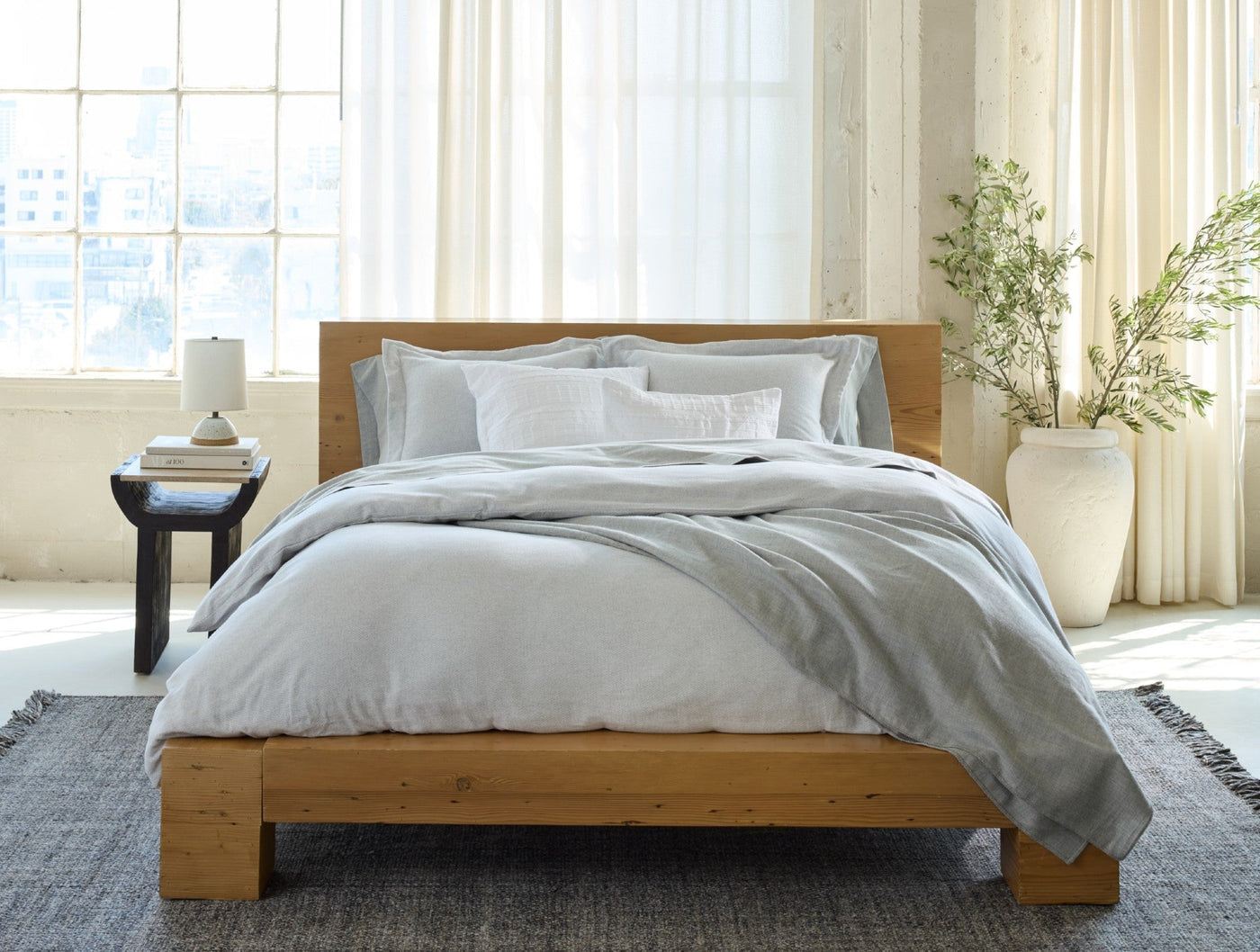 Heathered silver-grey blanket draped over a wood bed in a bright, airy bedroom.