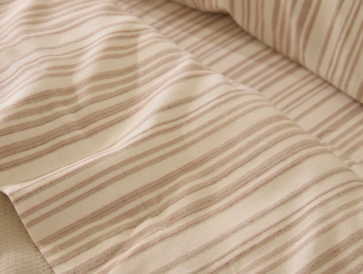 Close-up of Coyuchi Cloud Brushed Flannel in ivory with soft tan vertical stripes, draped fabric detail.