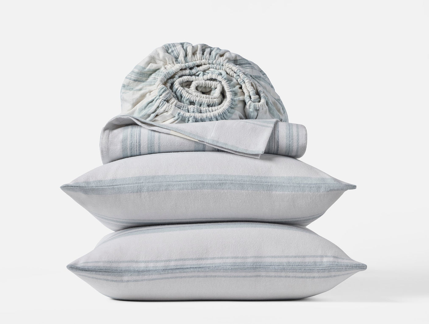 Close-up of two stacked Coyuchi Cloud Brushed Flannel pillowcases in muted blue stripe with rolled sheet on top.