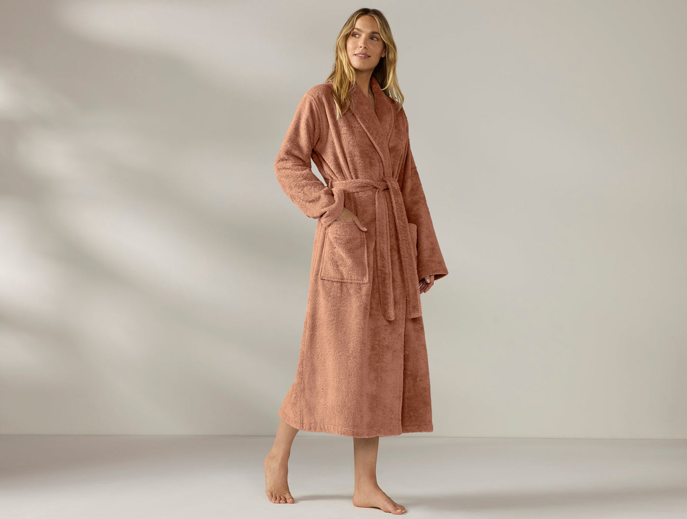 Model wearing long Coyuchi Cloud Loom robe in terracotta, belted waist, floor-length terry cloth.