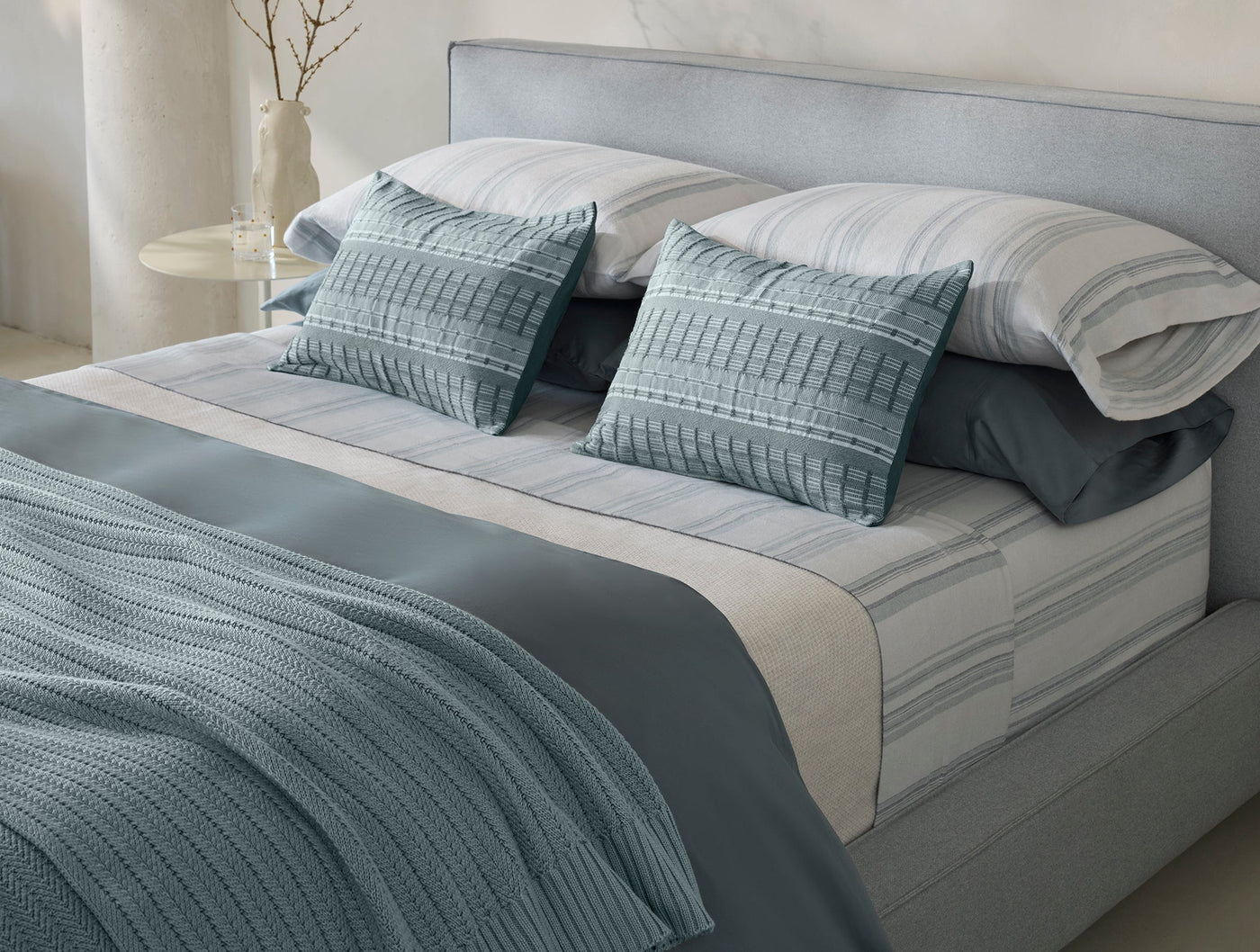 Seafoam knit throw draped across a styled bed with teal textured pillows.